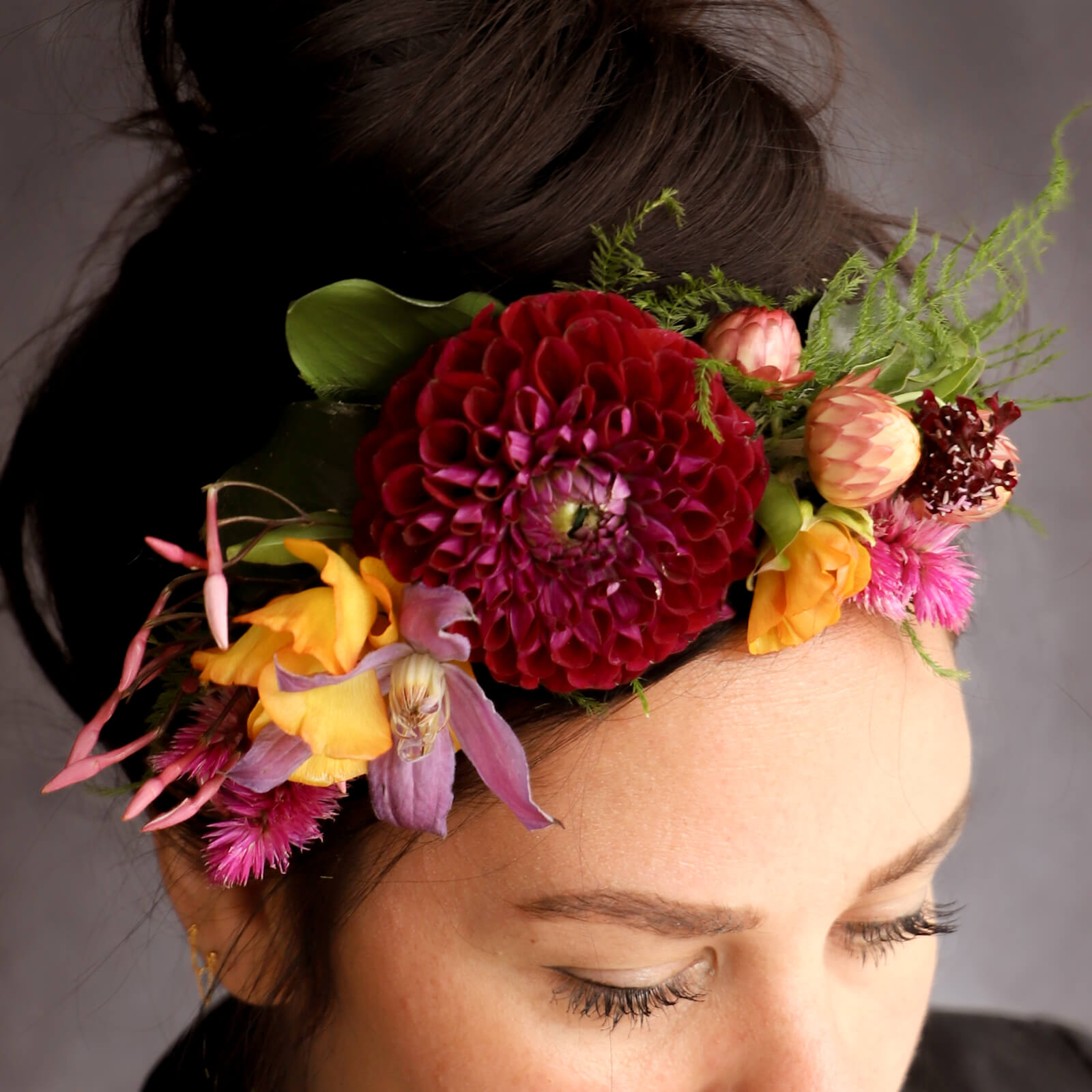 Model wearing a floral headband made of pink dahlias and yellow, orange and purple flowers. 